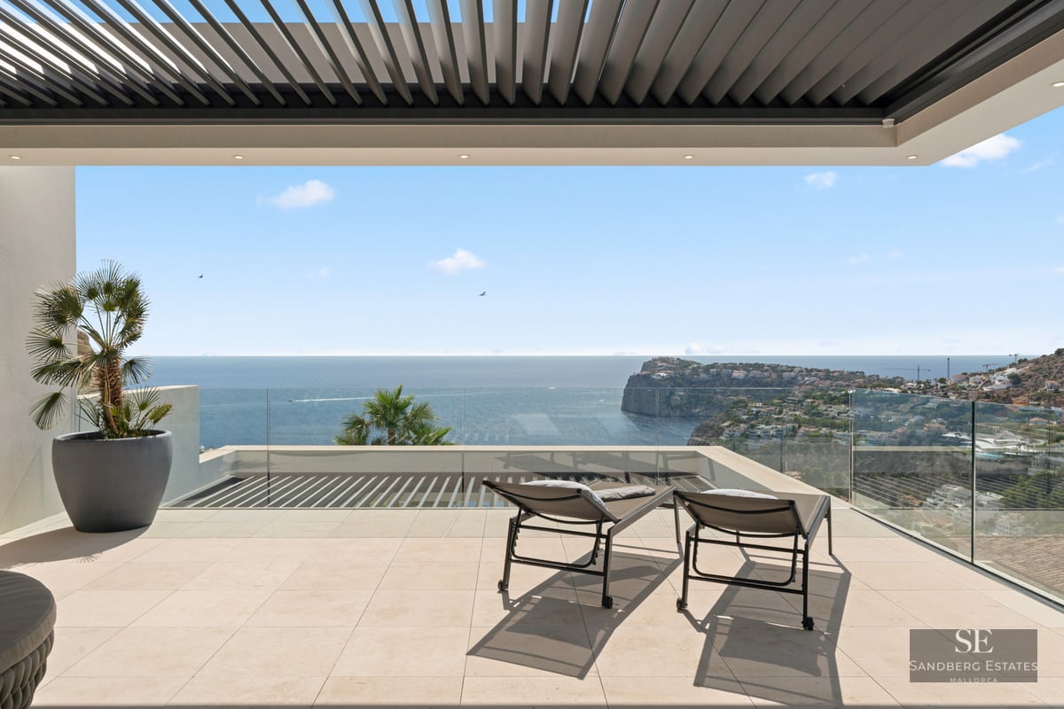 Modern terrace with glass railings, two sun loungers, and a wide view of the ocean and coastal cliffs.