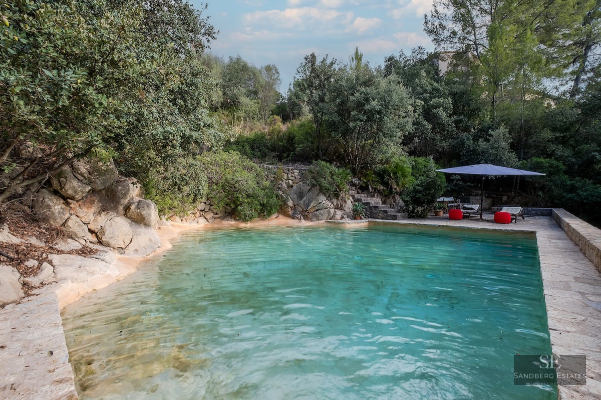 A lagoon-style pool with turquoise water, natural rock edges, and a lounge area with an umbrella and red accents.