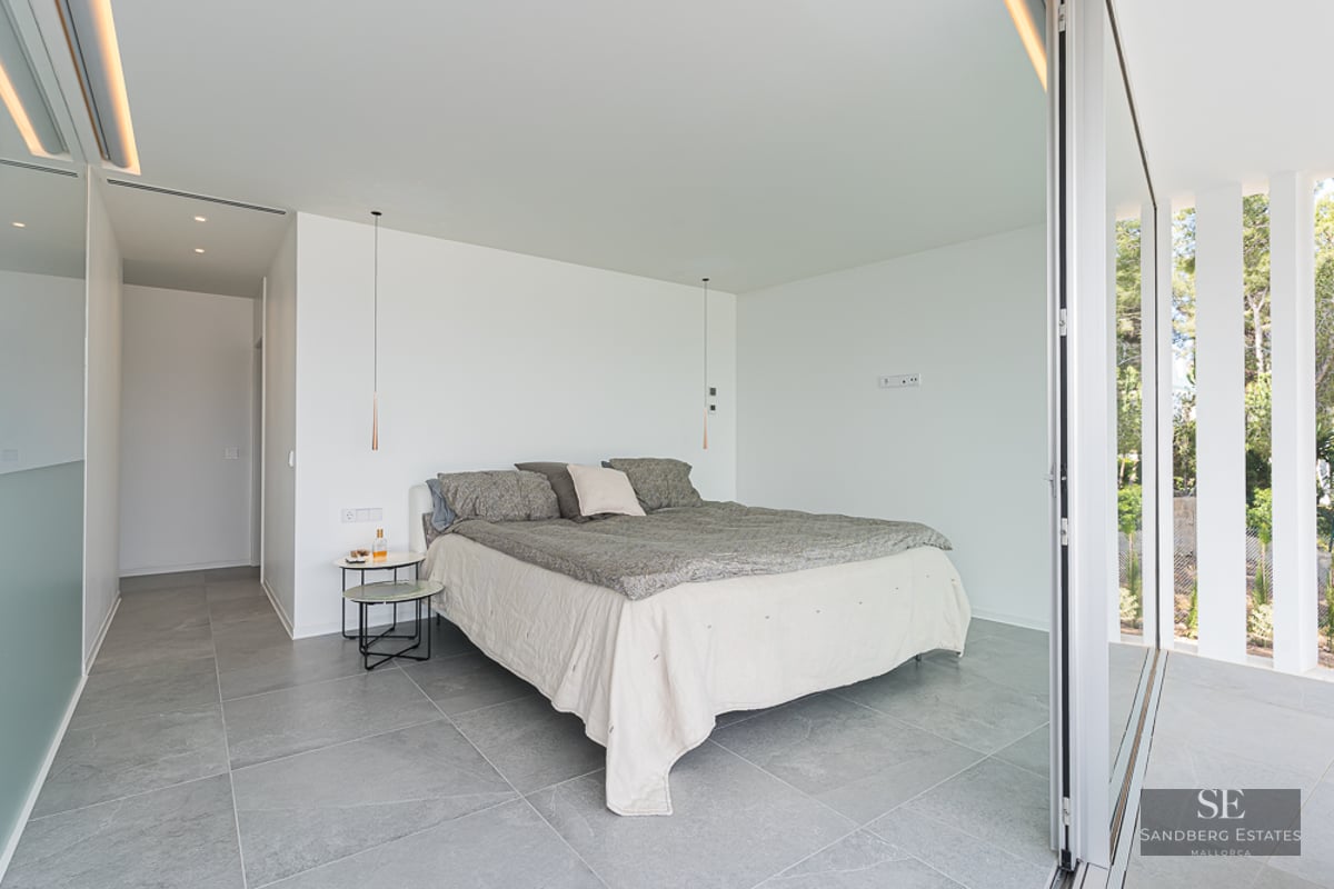 Minimalist bedroom with grey stone floors, white walls, and a large sliding glass door opening to a garden.