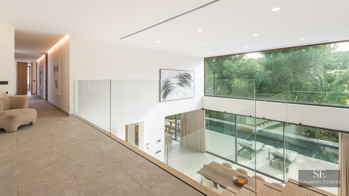 Vue depuis une mezzanine en verre sur un salon à double hauteur avec de grandes baies vitrées donnant sur la piscine.