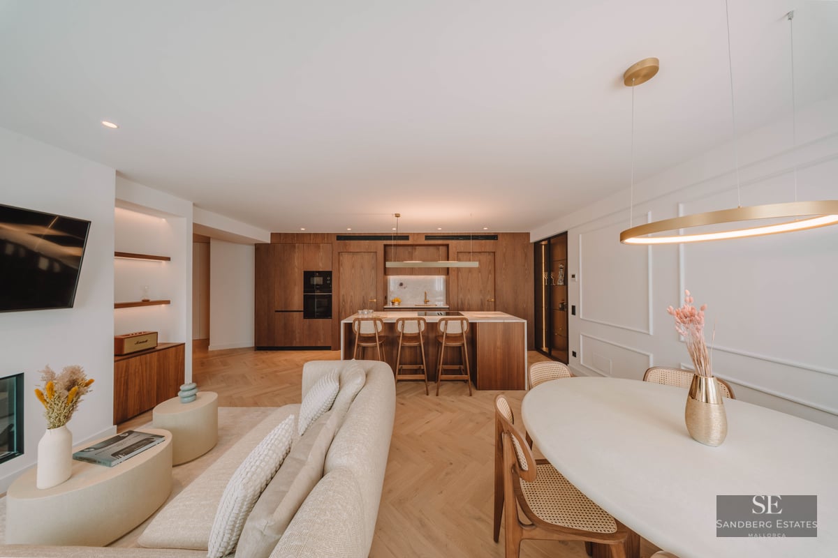 Spacious luxury living room featuring a beige sofa, herringbone wood floors, and an integrated natural wood kitchen.