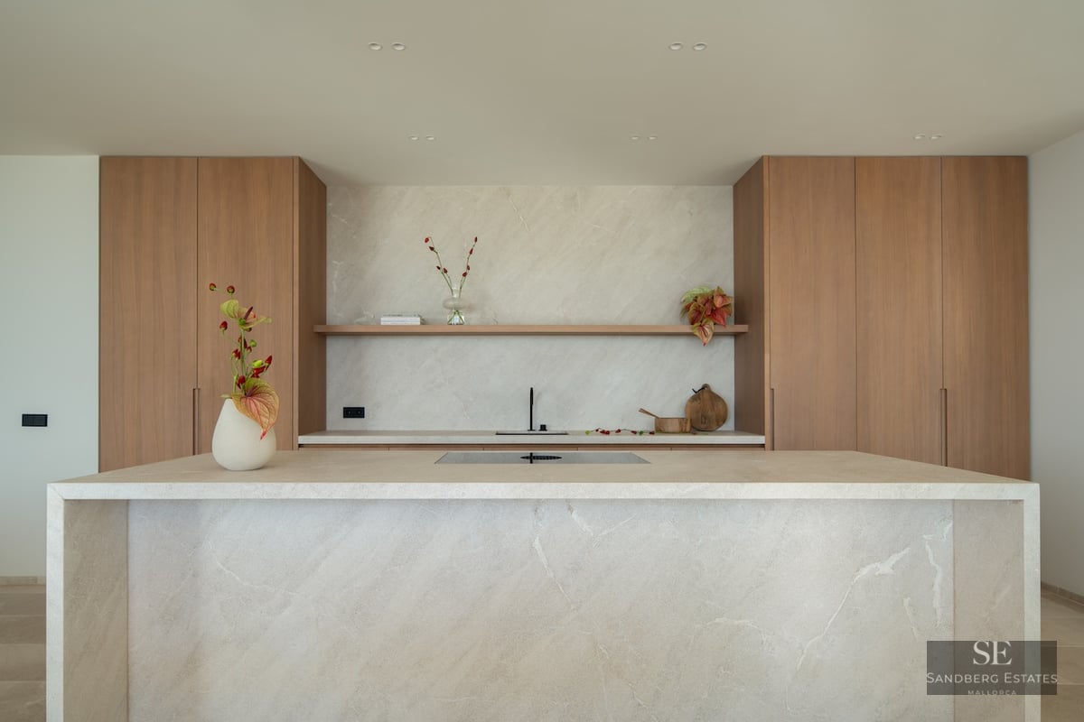 Modern kitchen featuring a large beige stone island, natural wood cabinets, and a matching stone backsplash.