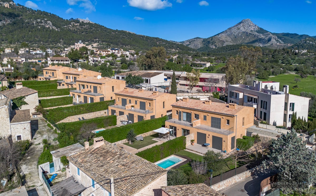 Aerial view of terracotta-colored villas with private pools and green hedges against a mountain backdrop.