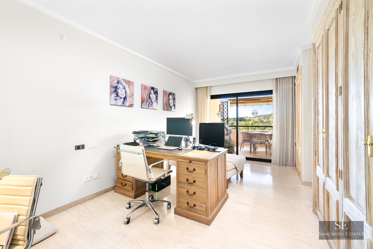 Bureau lumineux avec grand bureau en bois, chaise blanche et baies vitrées ouvrant sur une terrasse.