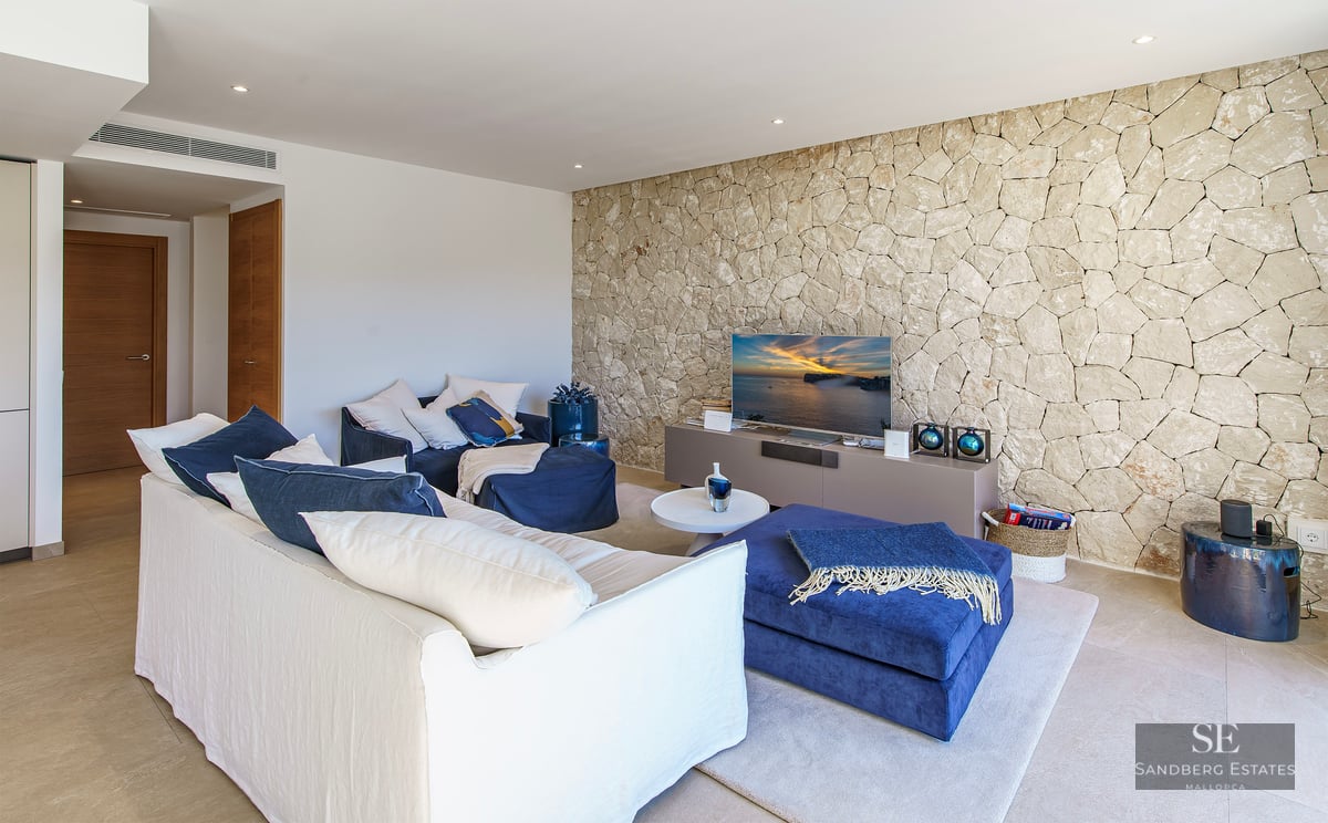 Contemporary living room featuring a white sofa, navy blue ottomans, and a textured natural stone wall with a TV.