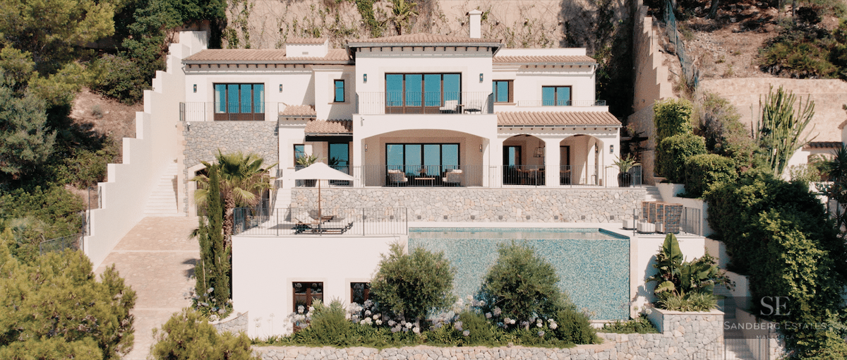 Exterior view of a multi-level white Mediterranean villa featuring a large infinity pool and stone accents.
