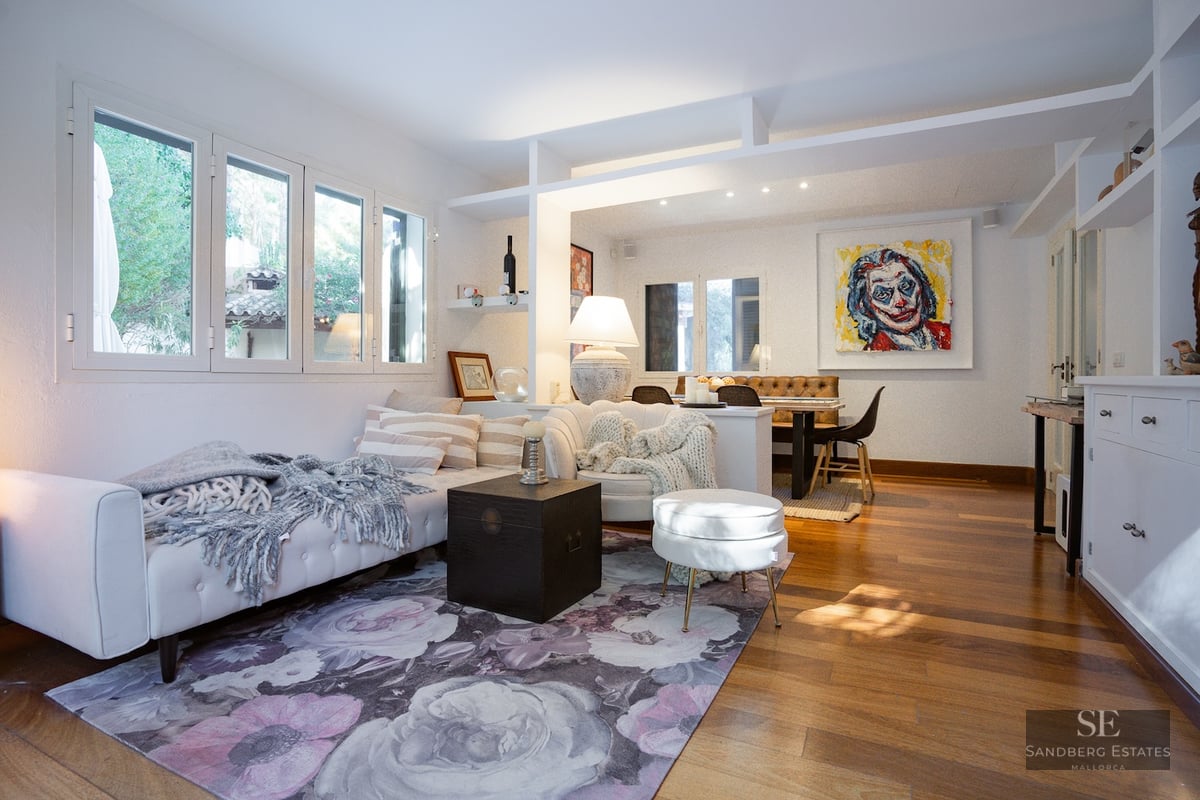 Open-plan living room with white sofas, floral rug, wood floors, and a dining area in the background.