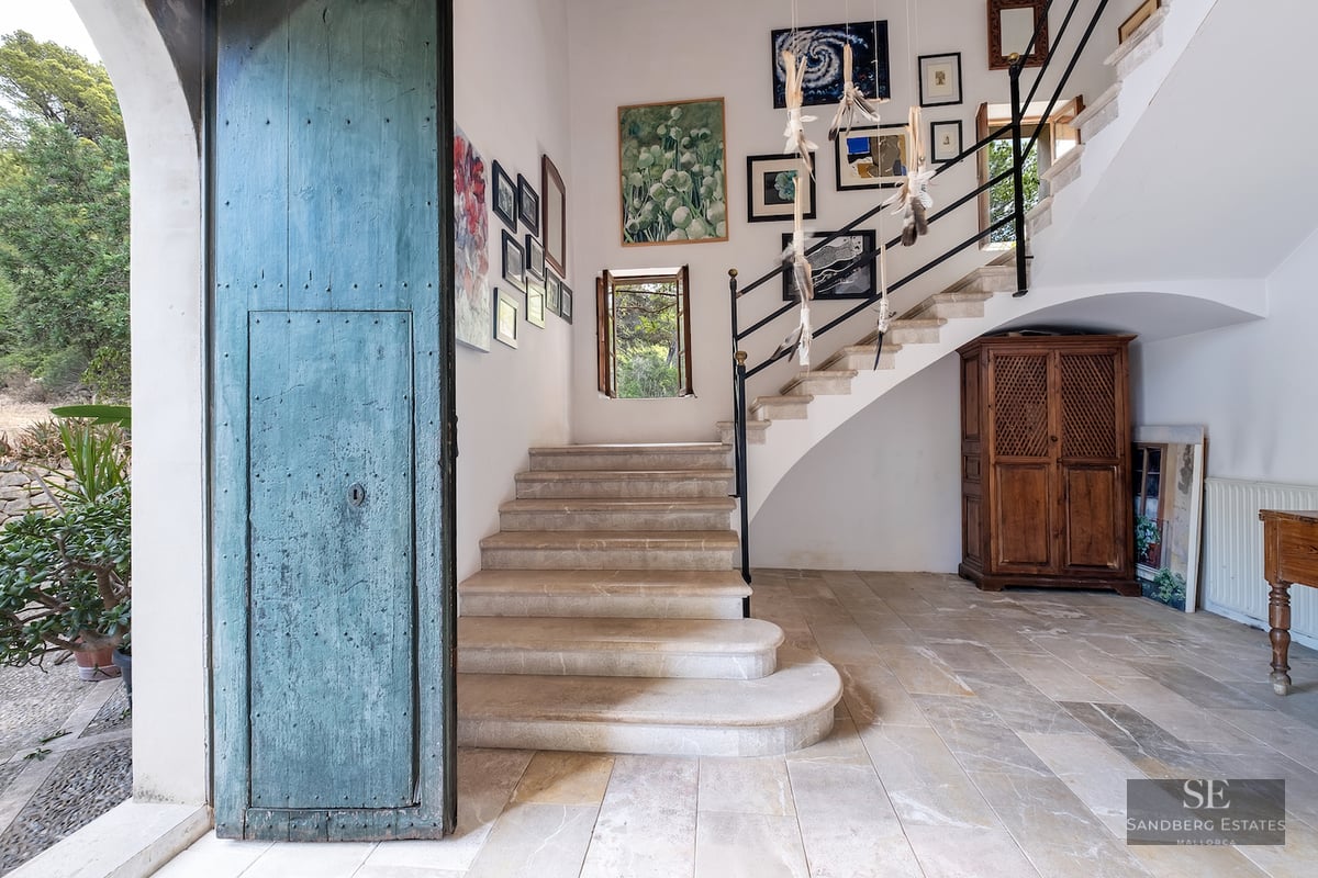 Entrance hall with a large distressed blue door, stone stairs leading up, and a gallery of paintings on white walls.