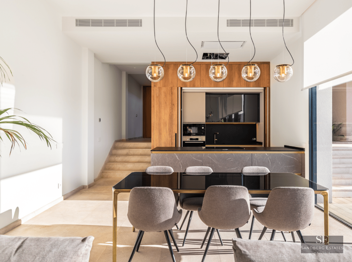 Modern dining room featuring a black glass table, grey chairs, designer pendant lights, and a marble kitchen island.
