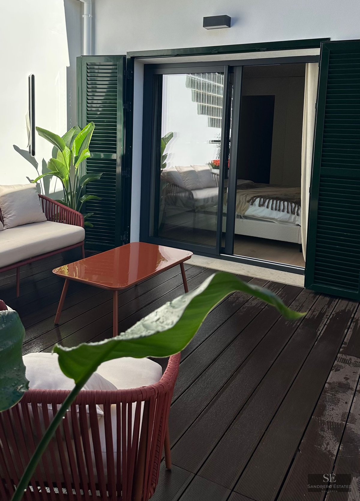 Private outdoor terrace with terracotta furniture, wooden decking, and green shutters next to a bedroom entrance.