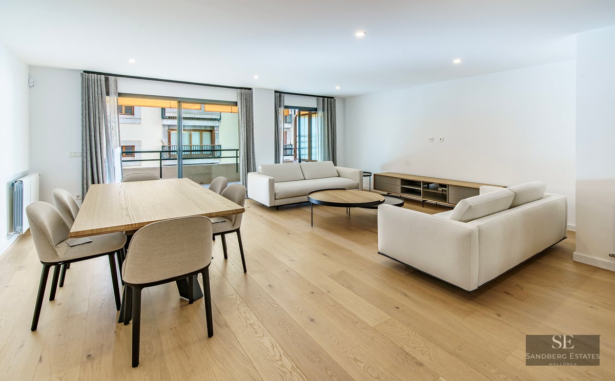 Séjour ouvert avec canapés blancs, table à manger en bois et grandes baies vitrées donnant sur un balcon.