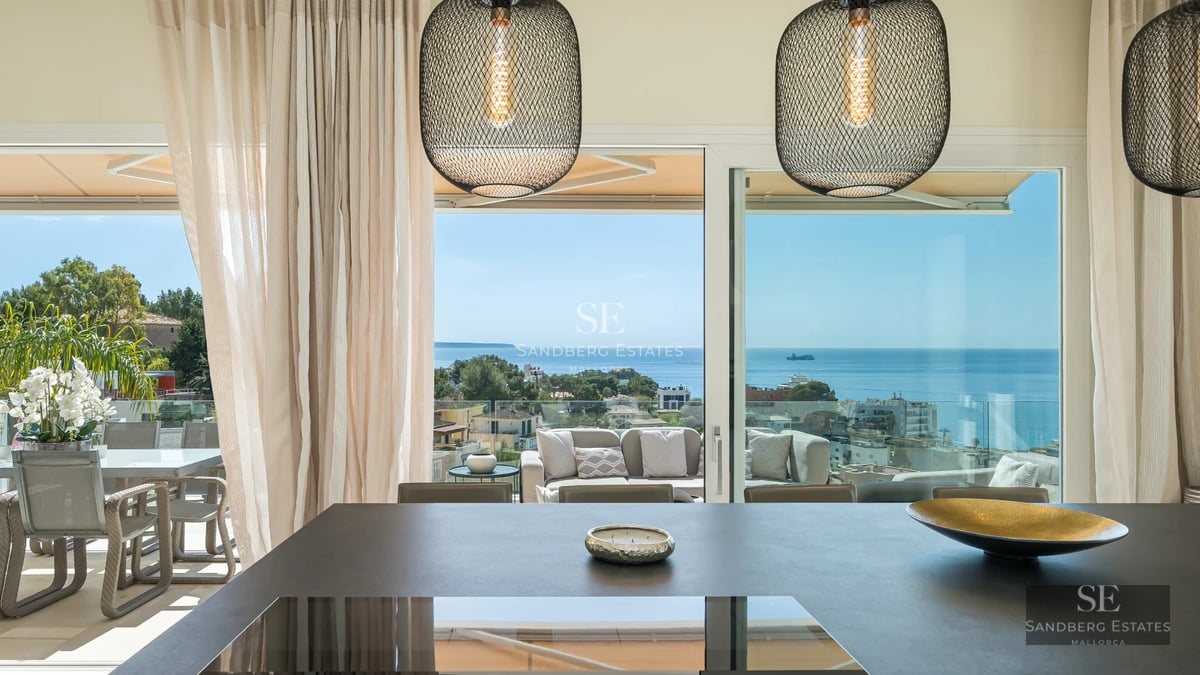 Exterior of a modern villa with a pool, lush greenery, and a large window reflecting sunlight.