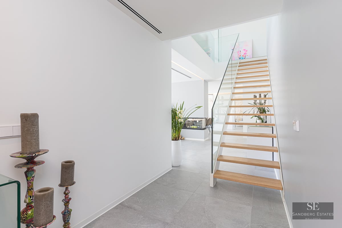 Bright modern hallway featuring a light wood floating staircase with glass railings and grey stone flooring.