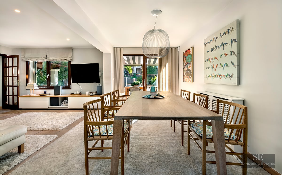 Wooden dining table with chairs under a spherical pendant light, open to the living room and outdoor terrace.