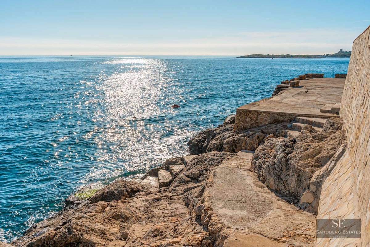 Stone terrace on a rocky coastline overlooking sparkling blue sea under bright sunlight.