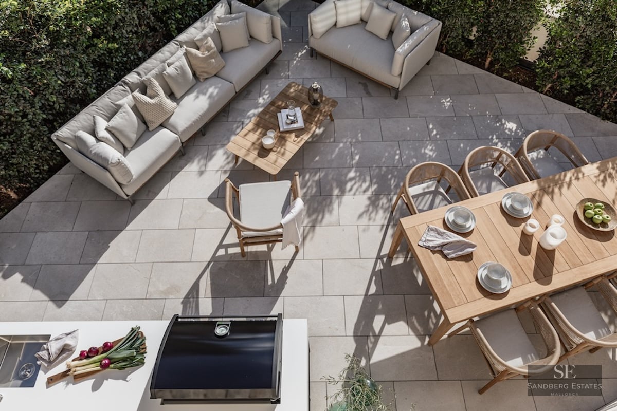 High-angle view of a stone-paved terrace with designer sofas, wooden dining table, and outdoor kitchen area.