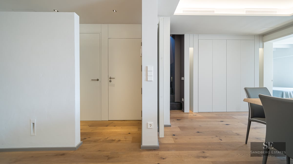 Modern hallway featuring white walls, minimalist doors, and light oak hardwood flooring.