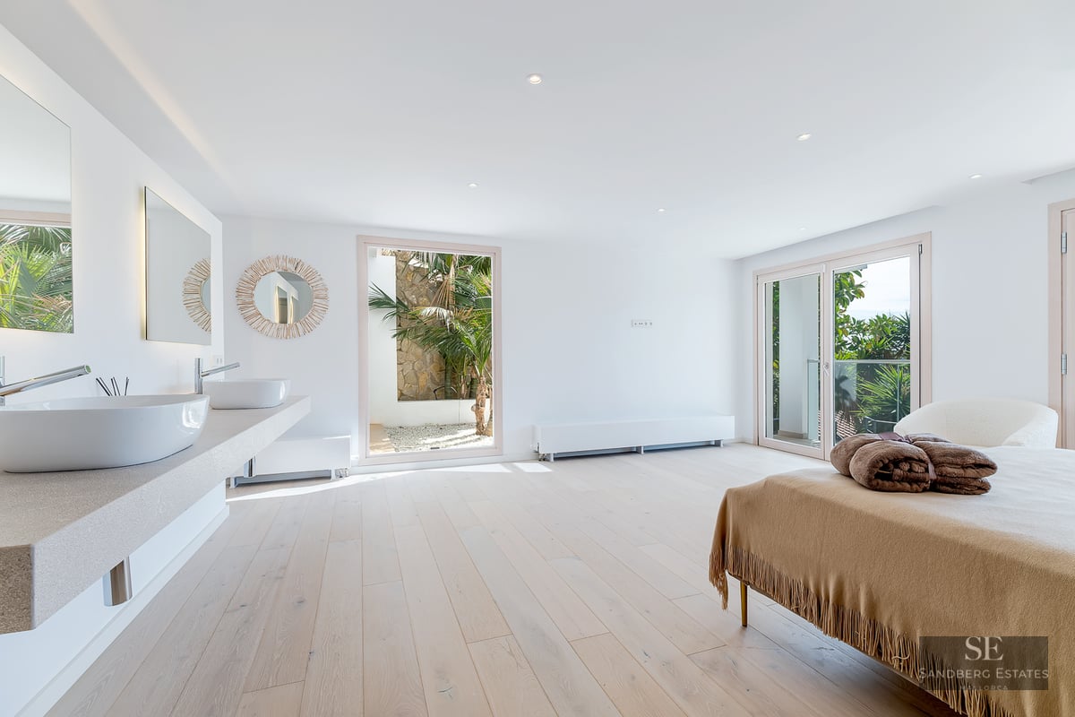 Bright master bedroom featuring light wood floors, a double vanity with vessel sinks, and glass doors to a garden.