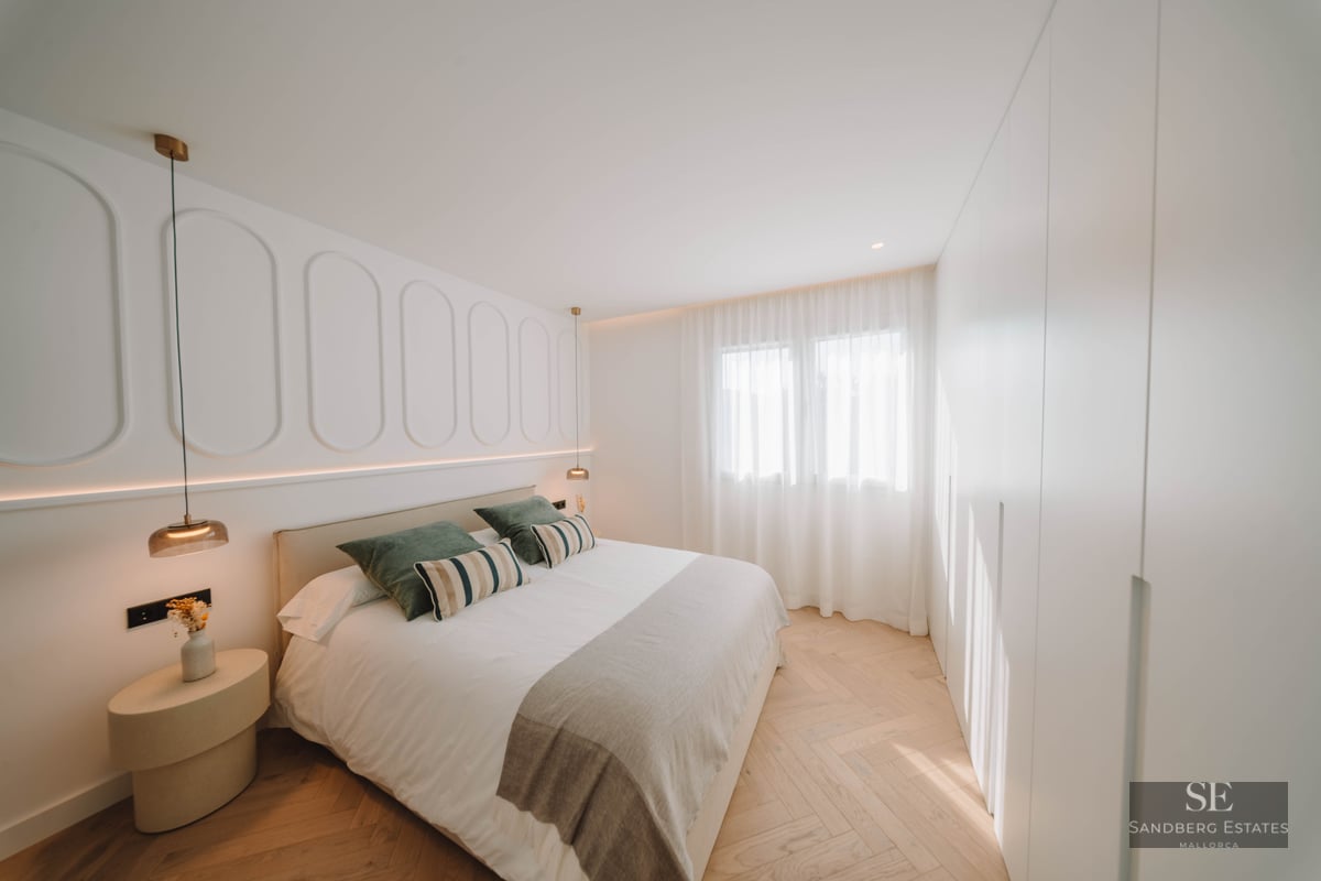 Modern master bedroom featuring a double bed, decorative wall molding, and light wood herringbone floors.