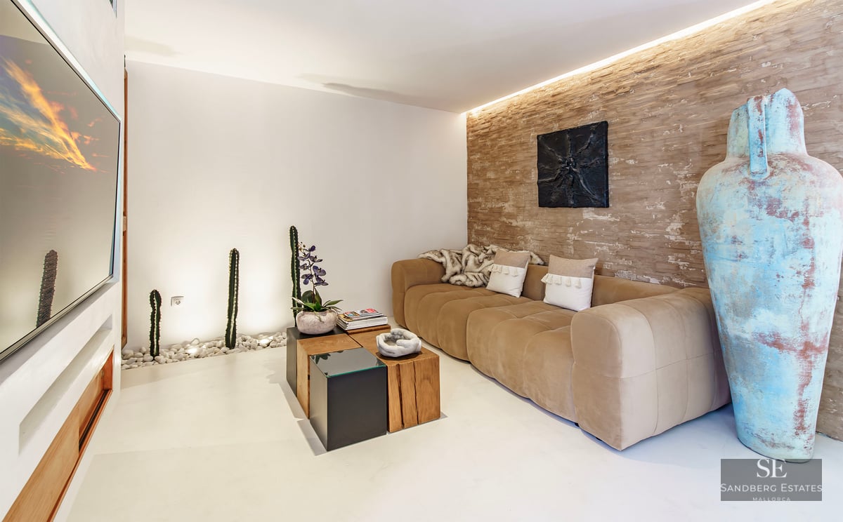 Modern lounge featuring a tan sofa, rustic stone accent wall, large turquoise vase, and indoor cactus garden.