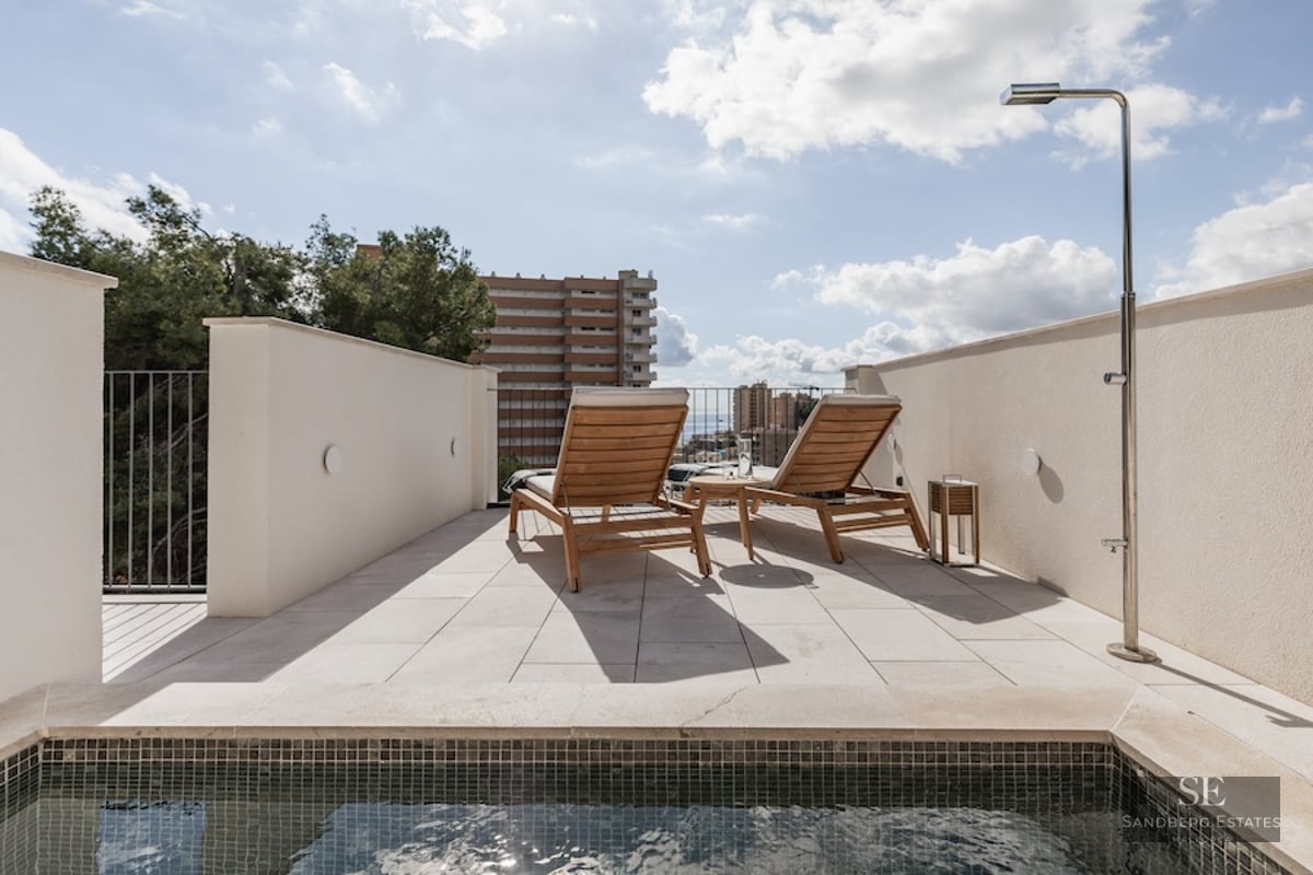 Sunny terrace featuring a small pool, two wooden loungers, and an outdoor shower under a bright blue sky.