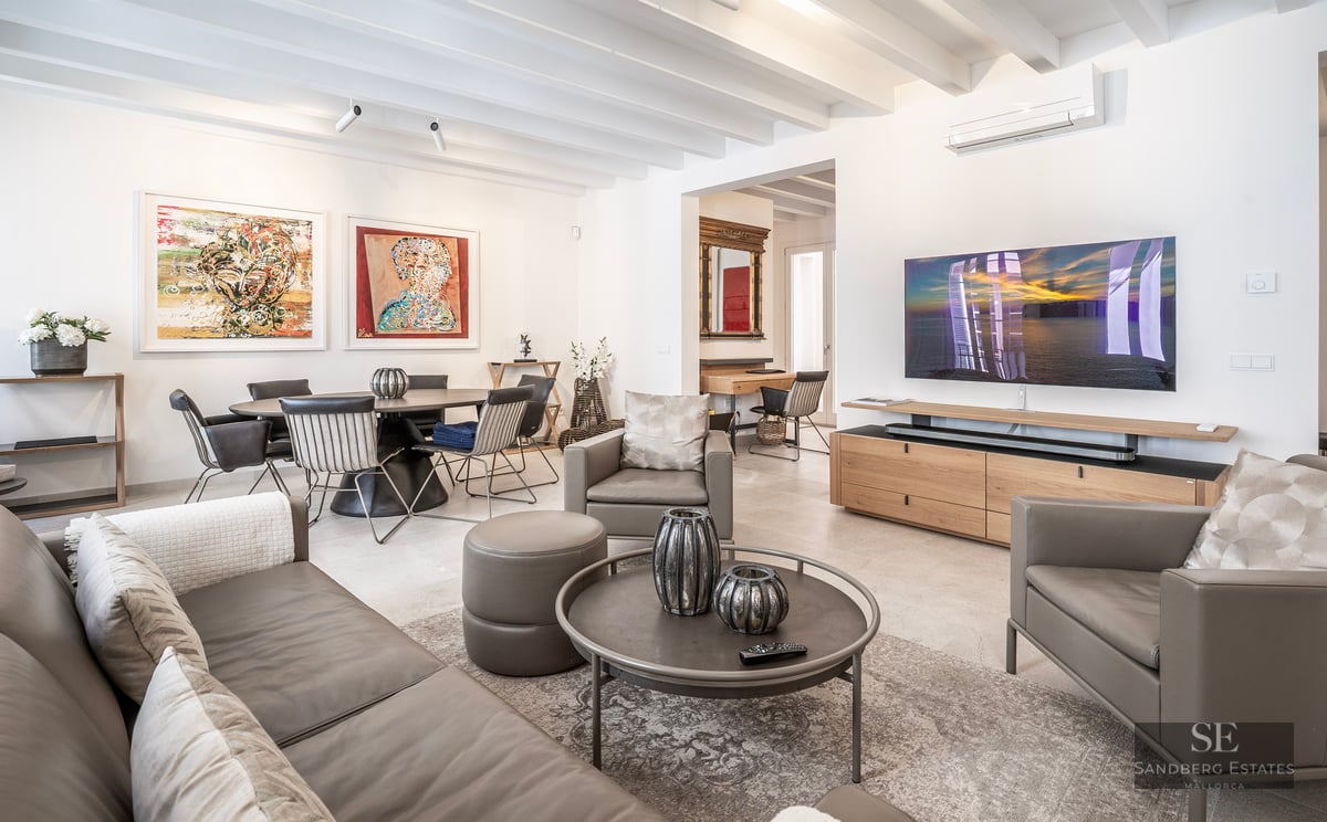 Spacious modern living room with grey leather sofas, wooden ceiling beams, large TV, and adjacent dining area with art.