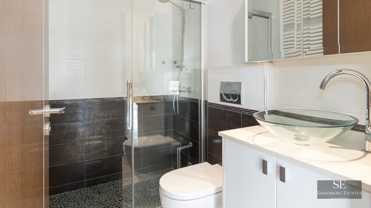 Modern bathroom featuring a glass bowl sink, white vanity, and a glass-enclosed shower with pebble tile floor.