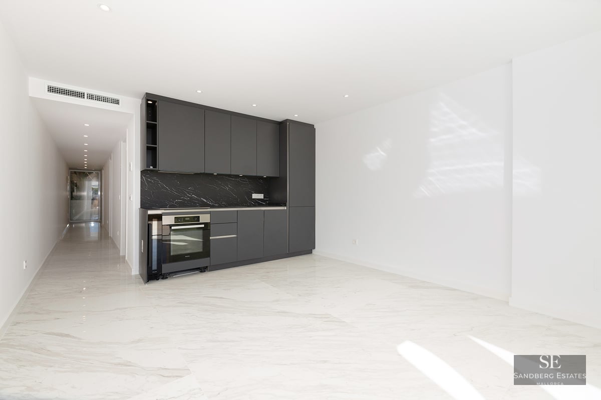 Modern kitchen area with dark gray cabinets, black marble backsplash, and white marble floors in a bright open room.