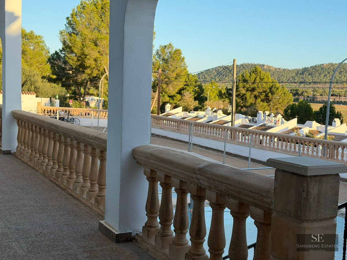 View from a stone balustrade balcony overlooking a Mediterranean neighborhood with white houses and green hills.