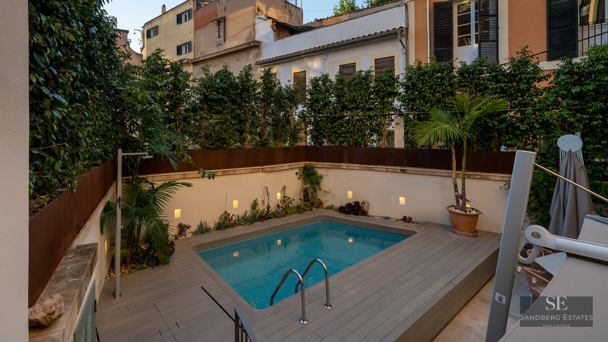 Modern rectangular pool with grey decking, surrounded by white walls with integrated lighting and lush greenery.