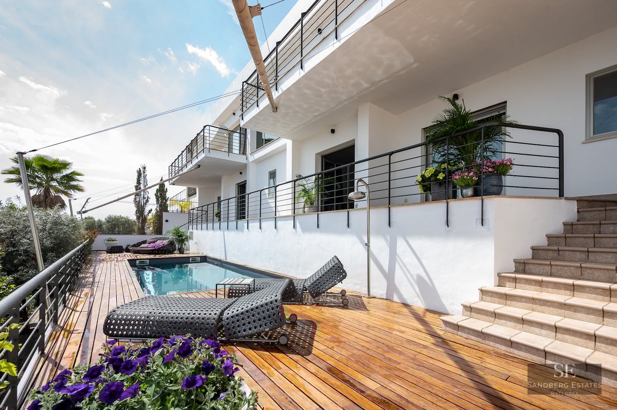 A modern swimming pool area with a wooden deck, loungers, and white architectural facade with black railings.