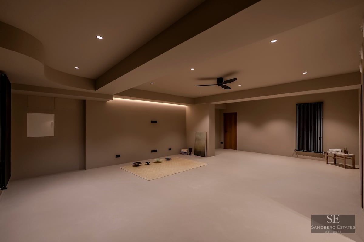 Une grande pièce minimaliste aux murs et sols beiges, avec éclairage encastré et ventilateur de plafond.