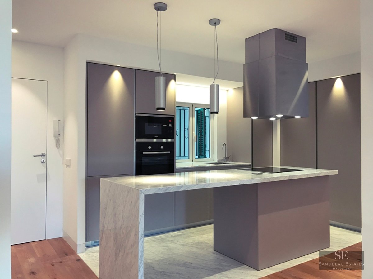 Modern kitchen featuring a purple island with a marble countertop, sleek cabinets, and designer pendant lighting.