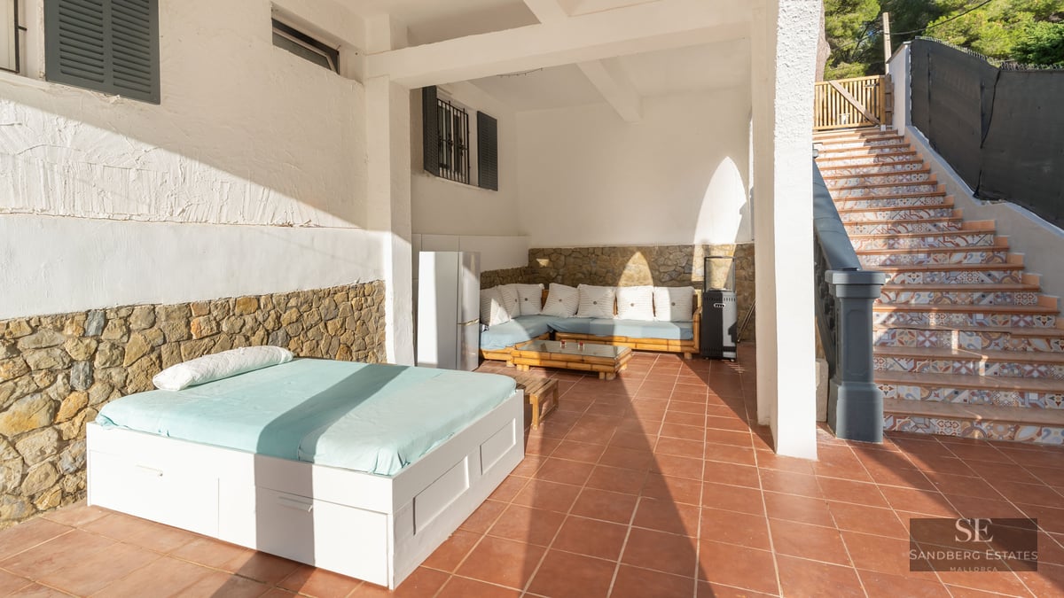 Terrasse couverte avec sols en terre cuite, lit de jour extérieur, banquette, murs en pierre et escalier carrelé.