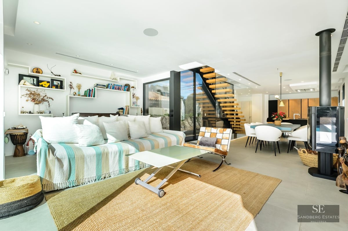 Bright modern living room with a striped sofa, floating wooden stairs, and a black freestanding fireplace.