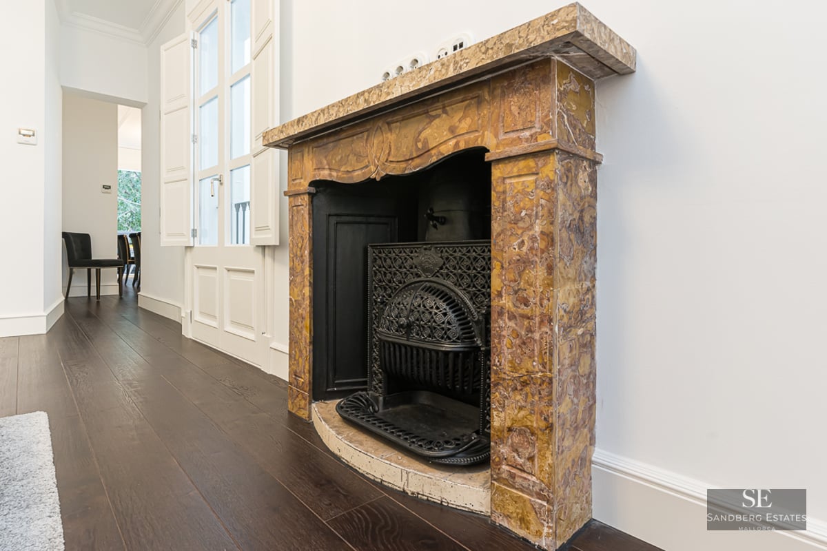 Ornate yellow marble fireplace with a decorative black cast iron grate on dark wood flooring against white walls.