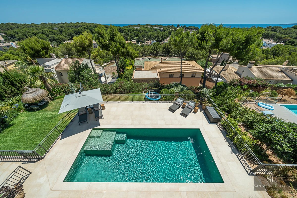 Vaste piscine avec vue, entourée de verdure. Design moderne, transats et parasols. Façade élégante et minimaliste.