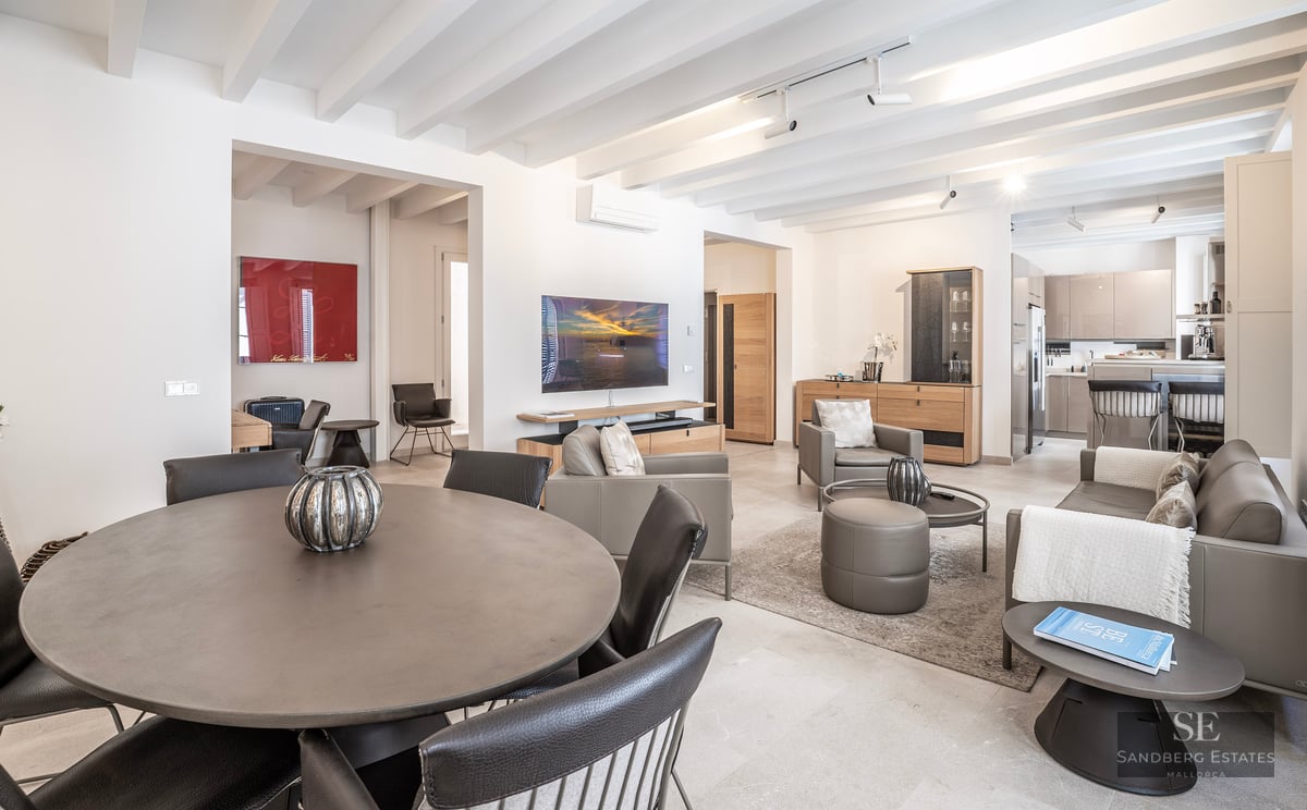 Modern open-plan living area with a round dining table, leather sofas, and white beamed ceiling.