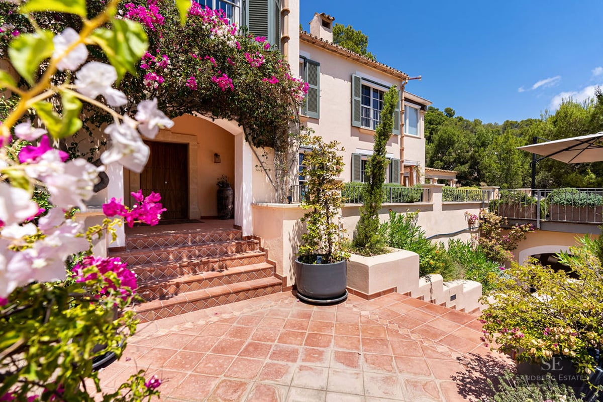 Terracotta steps leading to a wood door of a Mediterranean villa framed by pink bougainvillea.