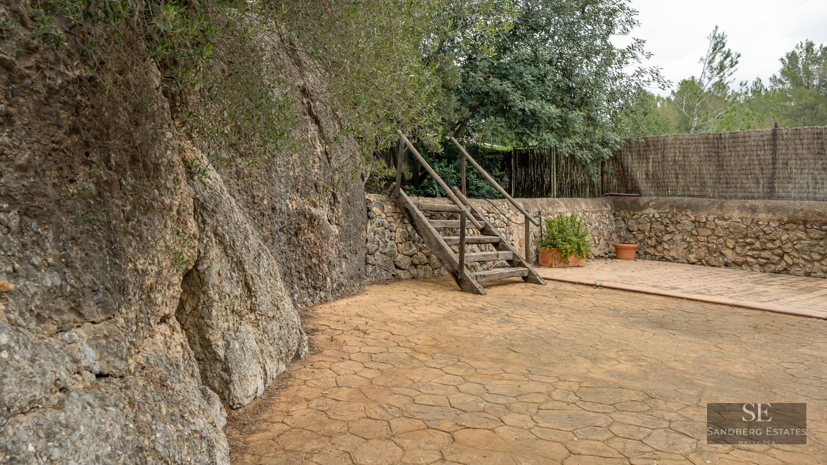 Rustic outdoor patio featuring a natural stone cliff, wooden stairs, and lush green landscaping.