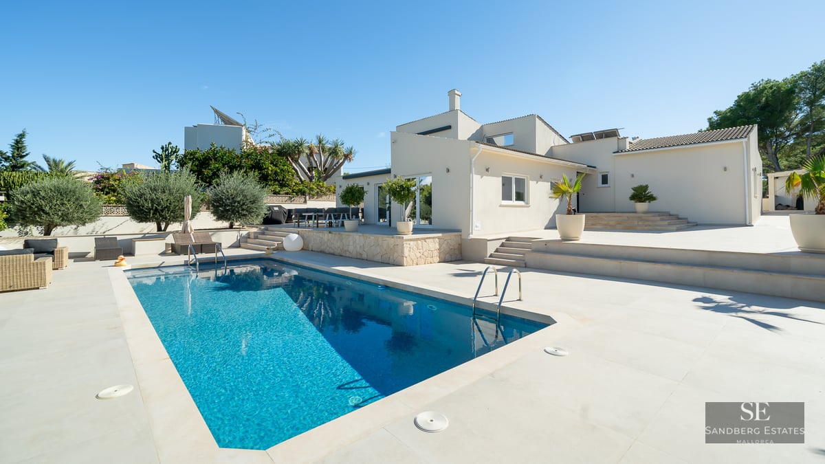 Piscine bleu éclatant à côté d'une villa blanche moderne avec une vaste terrasse en pierre sous un ciel dégagé.