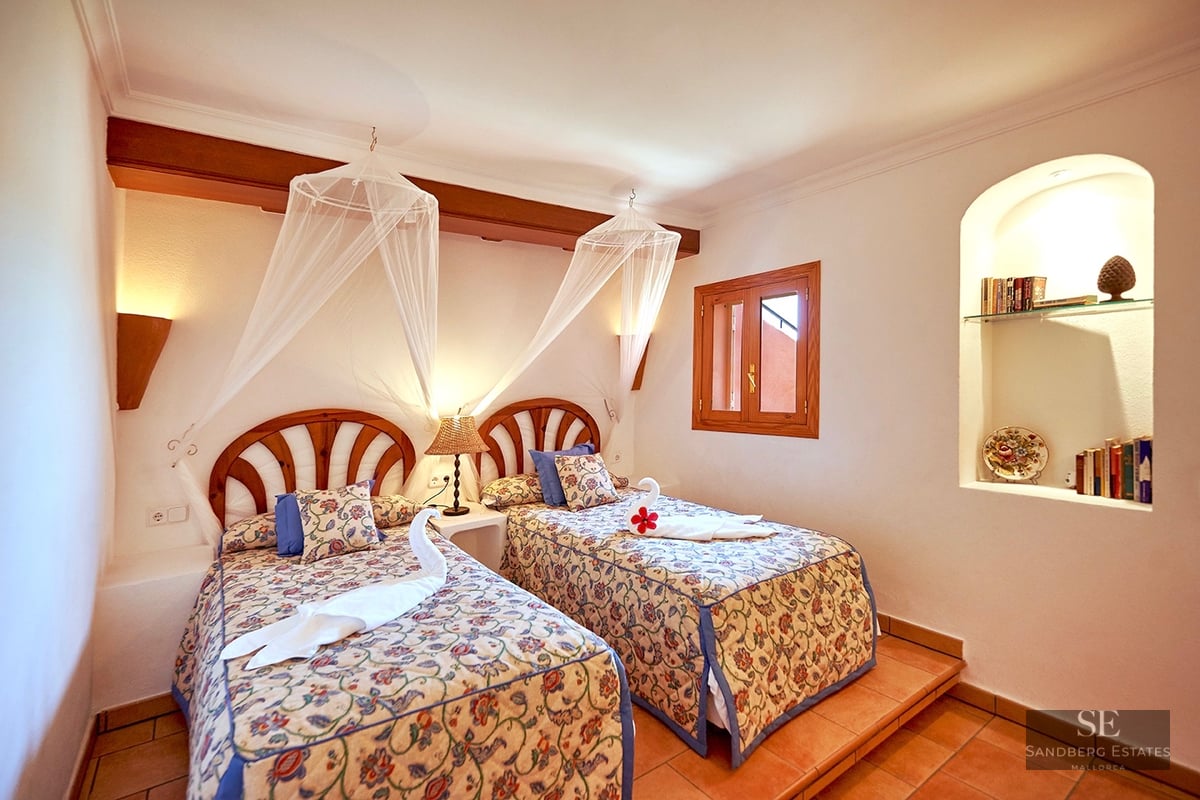 Two twin beds with floral covers and mosquito nets in a Mediterranean bedroom with terracotta floors.