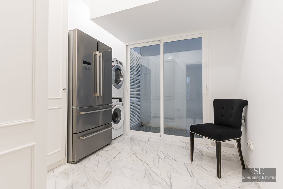 Utility room featuring a stainless steel refrigerator, stacked laundry unit, and white marble flooring.
