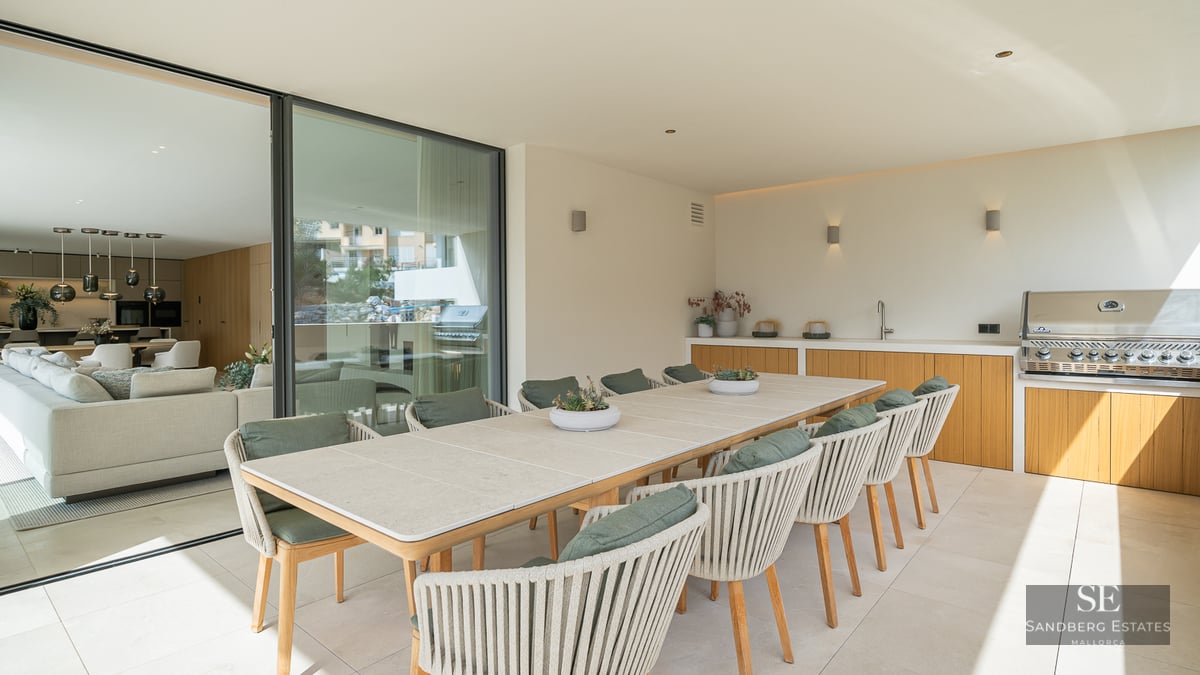 Large outdoor dining table with ten chairs next to an outdoor kitchen and grill on a modern covered terrace.