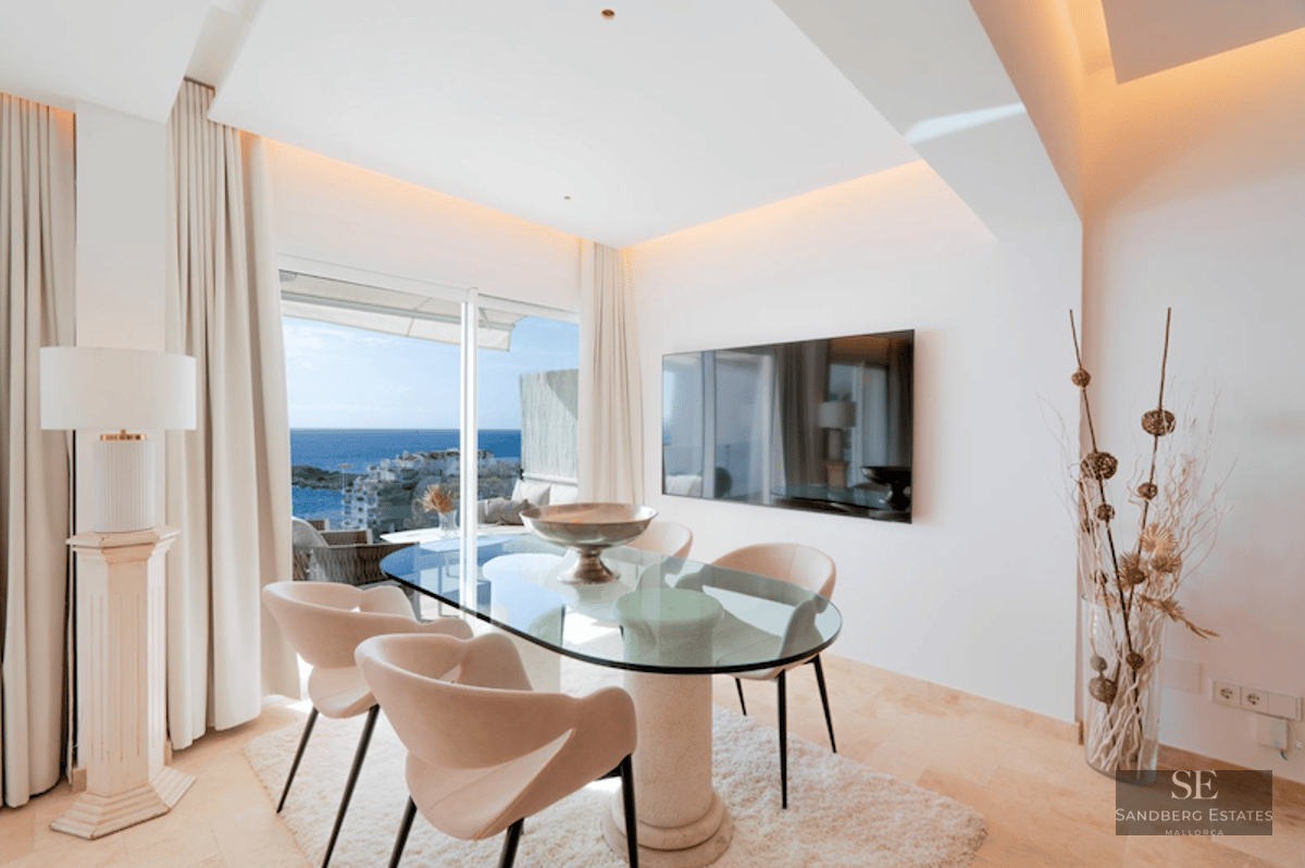 A modern dining room with a glass table, designer chairs, and large windows overlooking the Mediterranean sea.