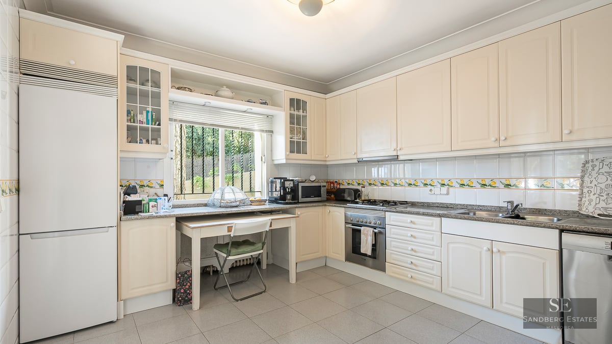 Spacious cream kitchen with granite counters, small dining table by a window, and integrated appliances.