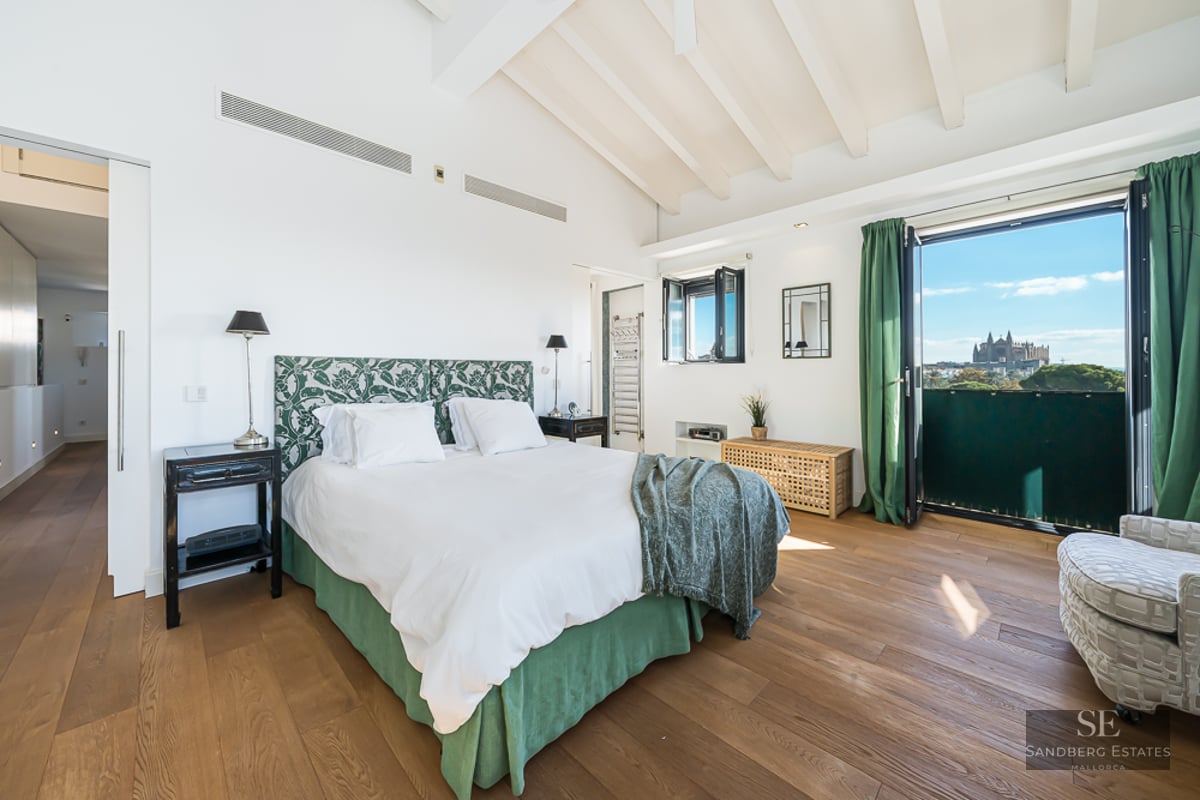 Bright master bedroom with high ceilings, white beams, and a balcony overlooking the Palma Cathedral.