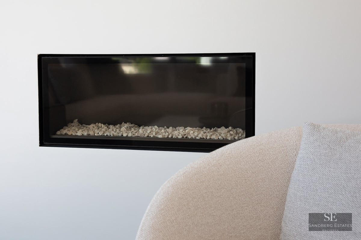 Close-up of a rectangular black-framed fireplace built into a white wall with white stones inside.