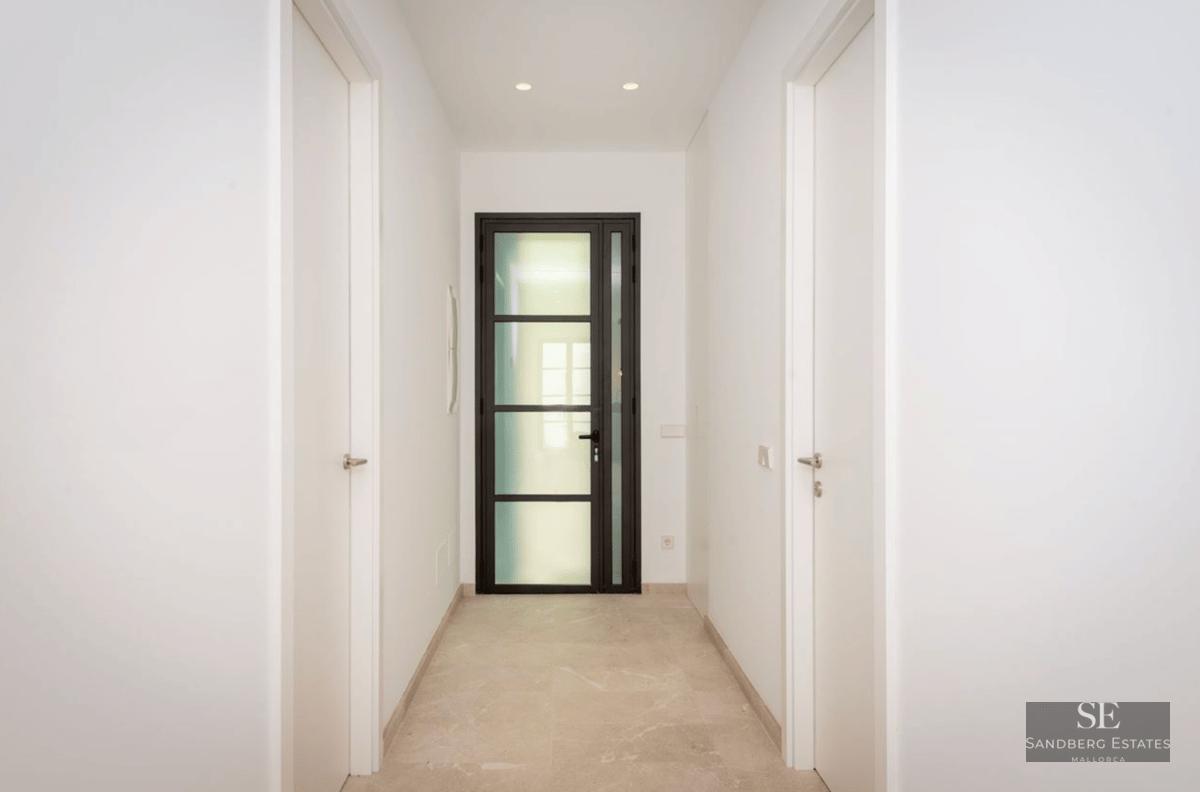 Narrow white hallway with polished stone floors leading to a black-framed glass door.