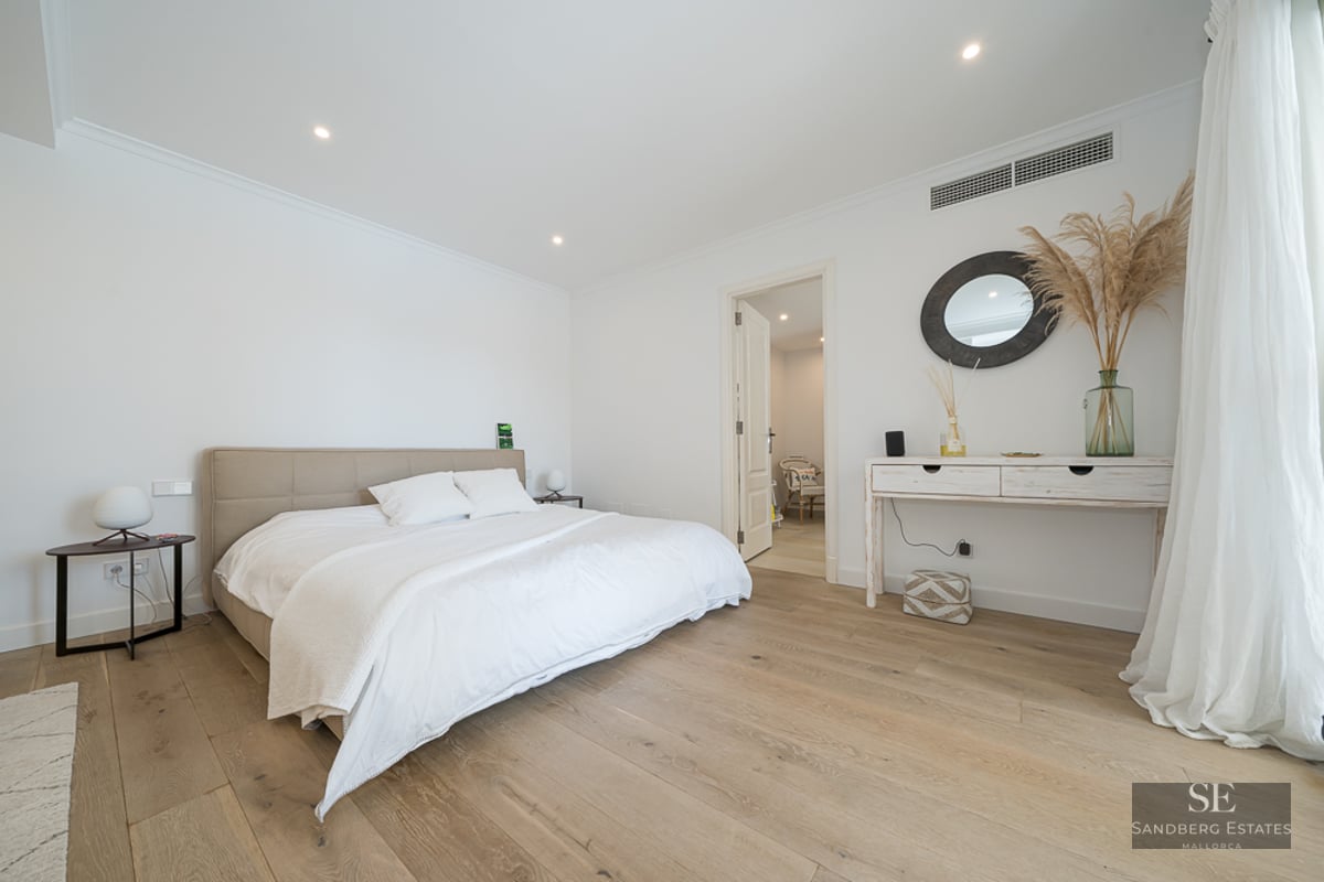 Chambre principale lumineuse avec lit blanc, parquet clair et console minimaliste avec miroir rond.